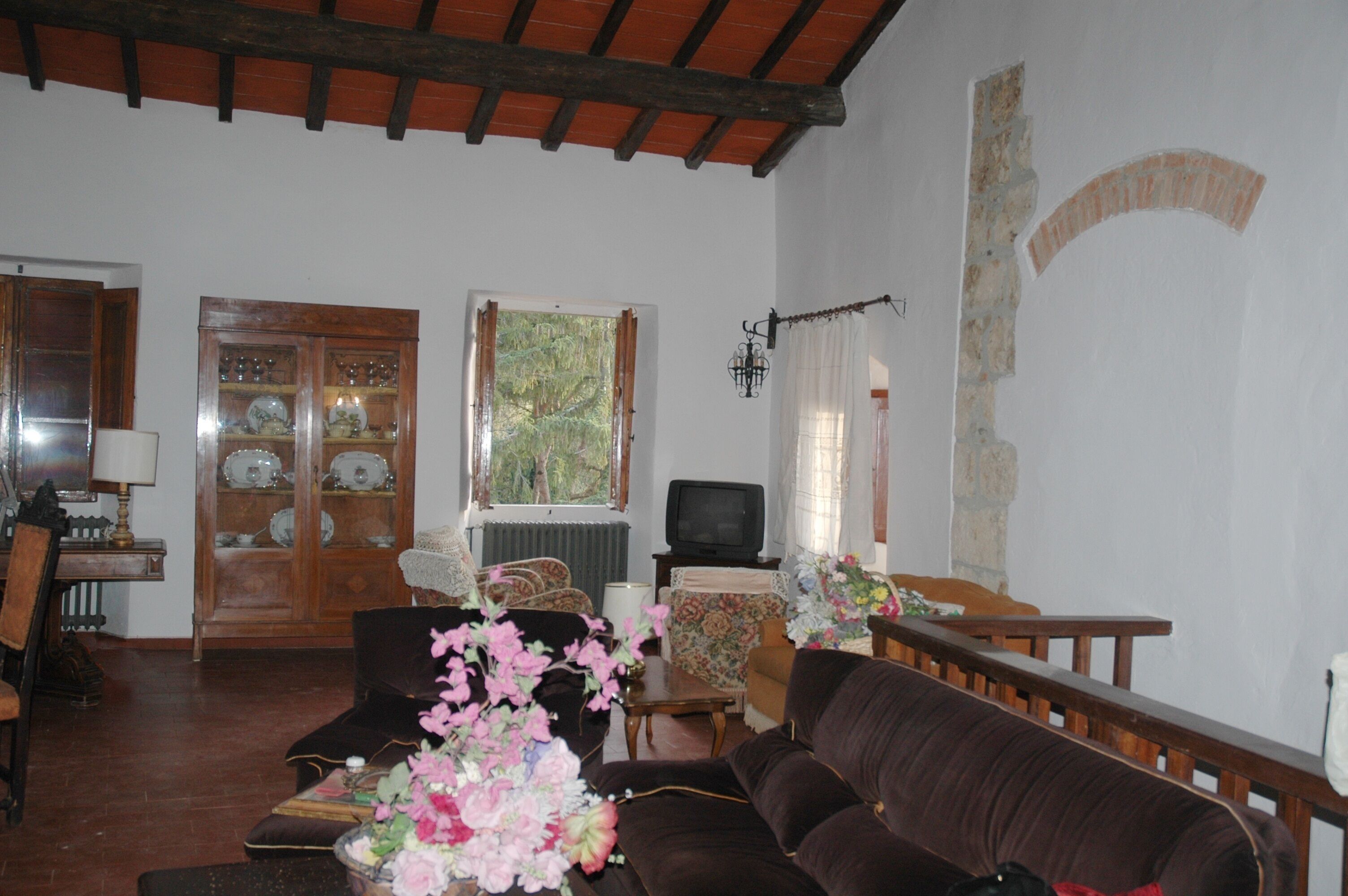 A living room with a brown sofa, a wooden cabinet with glass doors, a television, and a window with curtains.