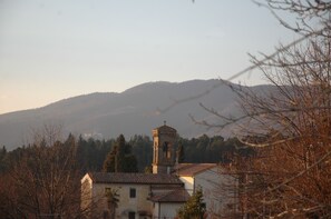 Une église dotée d’un clocher, entourée d’arbres et de collines.