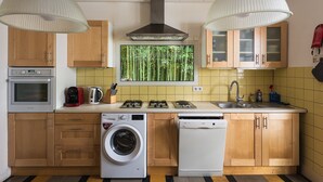 A modern kitchen with wooden cabinets, a built-in oven, a washing machine, a dishwasher, and a window with a bamboo view.