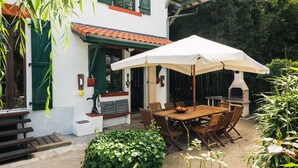 A patio with a table and chairs, a white umbrella, and a brick oven.