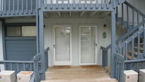 Une entrée d’immeuble avec deux portes portant les numéros 207 et 208, un escalier en bois et une rambarde bleue.