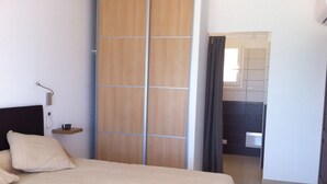 Quarto com cama, mesa de cabeceira, armário e banheiro visível através de uma porta aberta.