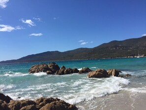 A coastal landscape with rocky shores, clear turquoise waters, and distant hills.