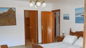 Un dormitorio con una cama de madera, una mesita de noche, una lámpara y dos puertas que dan a otras habitaciones.