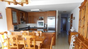 Una cocina con armarios de madera, una isla central y un comedor con sillas de madera.