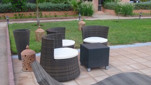 Eine Terrassenfläche mit Korbmöbeln, darunter eine Liege, zwei Stühle und ein kleiner Tisch.