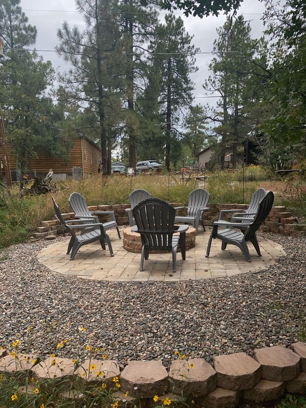 An outdoor seating area with Adirondack chairs and a fire pit, surrounded by a stone border and pebbles.
