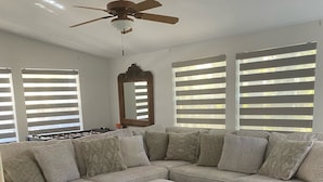 Una sala de estar con un sofá modular, un reposapiés a juego, un ventilador de techo y un espejo grande.
