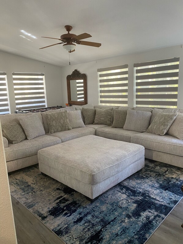 A living room with a sectional sofa, a matching ottoman, a ceiling fan, and a large mirror.