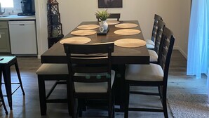 Un comedor con una mesa rectangular, seis sillas, un florero central con follaje y una lámpara en el techo.
