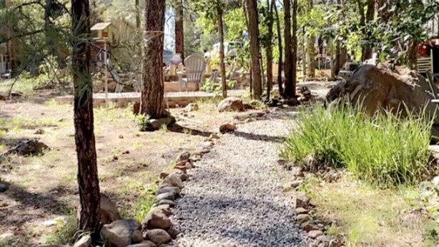 Un sendero de grava flanqueado por rocas, rodeado de árboles y follaje.