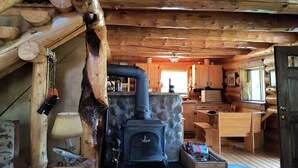 Interior rústico de una cabaña con chimenea de piedra, escalera de madera y zona de comedor.