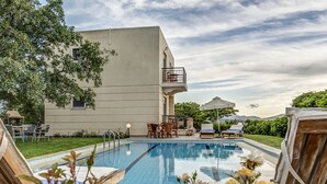 Ein Schwimmbad mit Liegestühlen und einem Tisch, umgeben von Grünflächen und einem Gebäude mit Balkon.
