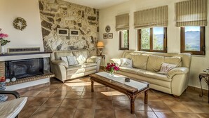 Ein Wohnzimmer mit Steinwand, zwei Sofas, einem Kamin und großen Fenstern mit Vorhängen.