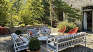 Un espace extérieur aménagé avec des meubles blancs, une plante en pot et un bâtiment en pierre en arrière-plan.