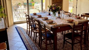 Un espace repas avec une grande table dressée pour six personnes, entourée de chaises en bois, sous un plafond voûté aux poutres apparentes.