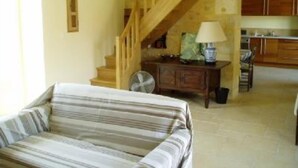 A cozy living room with a striped sofa, a wooden staircase, and a kitchen in the background. - La Boissière: Peaceful vacations in Périgord Noir (Saint Chamassy)