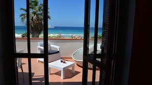 Un balcón con muebles blancos, vista a la playa y una palmera.