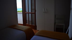 Una habitación con dos camas, un armario y vista al mar.