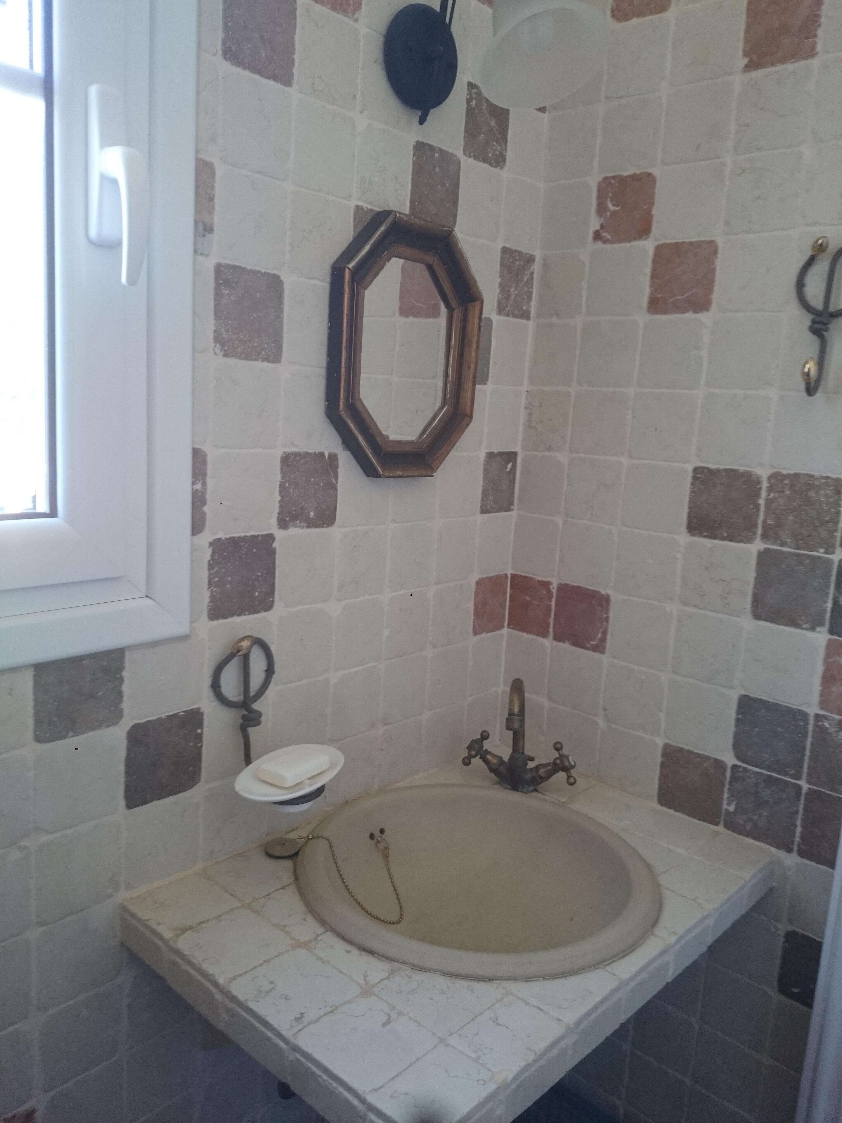 A bathroom with a tiled wall, a sink, a mirror, and a window.