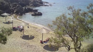 Ein Strand mit felsigem Gelände, Sonnenschirmen und einigen entspannten Personen.