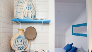 A bathroom with a blue shelf holding a vase and a mirror, and a bedroom with a bed, pillows, and a blue-framed mirror. - Apartment/ flat - Lisboa (Lisboa)