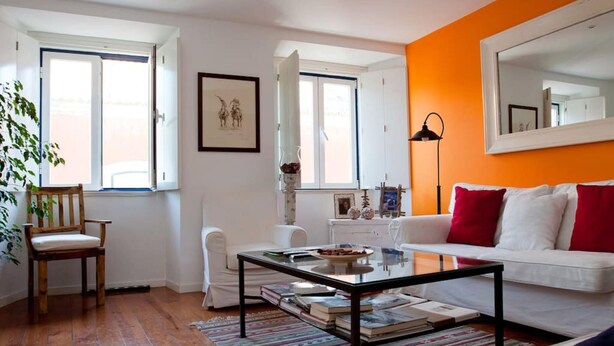 A living room with a white sofa, a glass coffee table, and a wooden chair. There are two windows with white frames and a door. - Apartment/ flat - Lisboa (Lisboa)