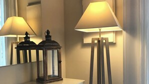 Ein Zimmer mit weißem Schminktisch, einem Spiegel, einer Stehlampe und einem kleinen Tisch mit einer Laterne.