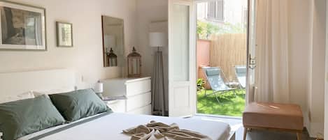 A bedroom with a bed, bedside table, lamp, and a view of the garden.