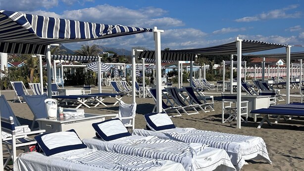 Ein Strandloungebereich mit Liegestühlen, Sonnenschirmen und einer überdachten Sitzgelegenheit.