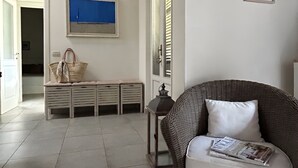 Ein Zimmer mit einem Korbssessel, einer Bank mit einem Korb, einem gerahmten Bild und einer Tür mit Rollläden.