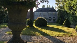 A large stone planter with flowers, a well-manicured lawn, and a stately building with a symmetrical facade and multiple chimneys. - Beautiful cottage with pool , LOIRE VALLEY close to ORLEANS .1 hour from Paris . (Saint-Jean-De-Braye)