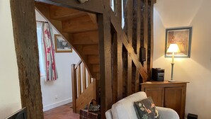 A cozy living room with a wooden staircase, a cushioned armchair, a lamp, and a framed picture on the wall. - Beautiful cottage with pool , LOIRE VALLEY close to ORLEANS .1 hour from Paris . (Saint-Jean-De-Braye)