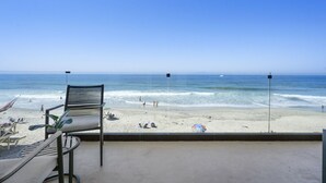 Uitzicht op het strand vanaf een balkon, met een stoel en een tafel, met zicht op de oceaan en mensen op het strand.