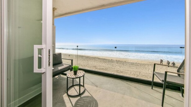 Een balkon met uitzicht op het strand, een bank, een kleine tafel met een plant en een glazen deur.