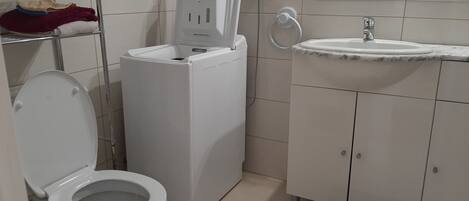 A compact bathroom with a toilet, a washing machine, and a sink.