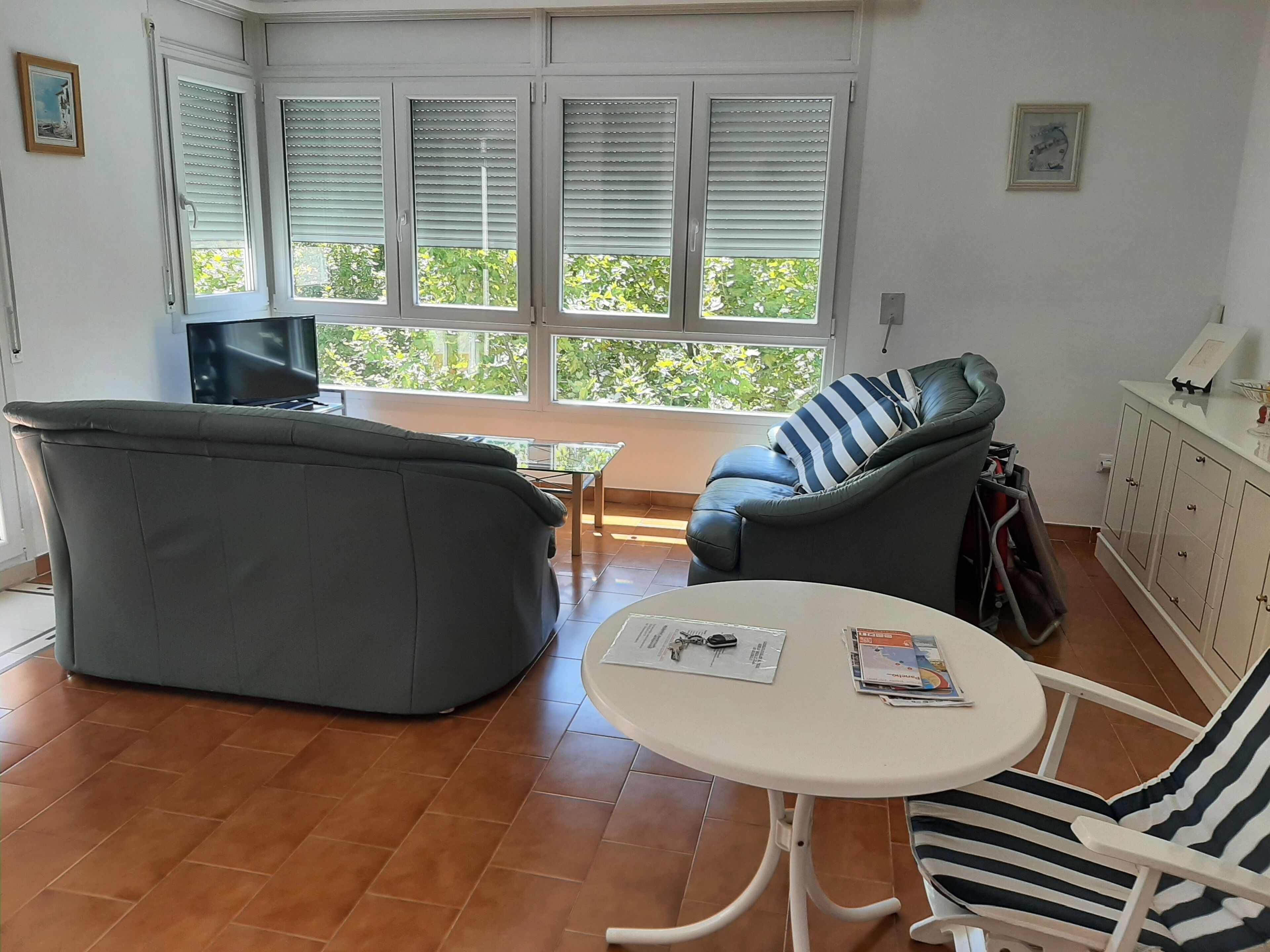 Un salon avec un canapé gris, un fauteuil à rayures, une petite table ronde et un téléviseur.