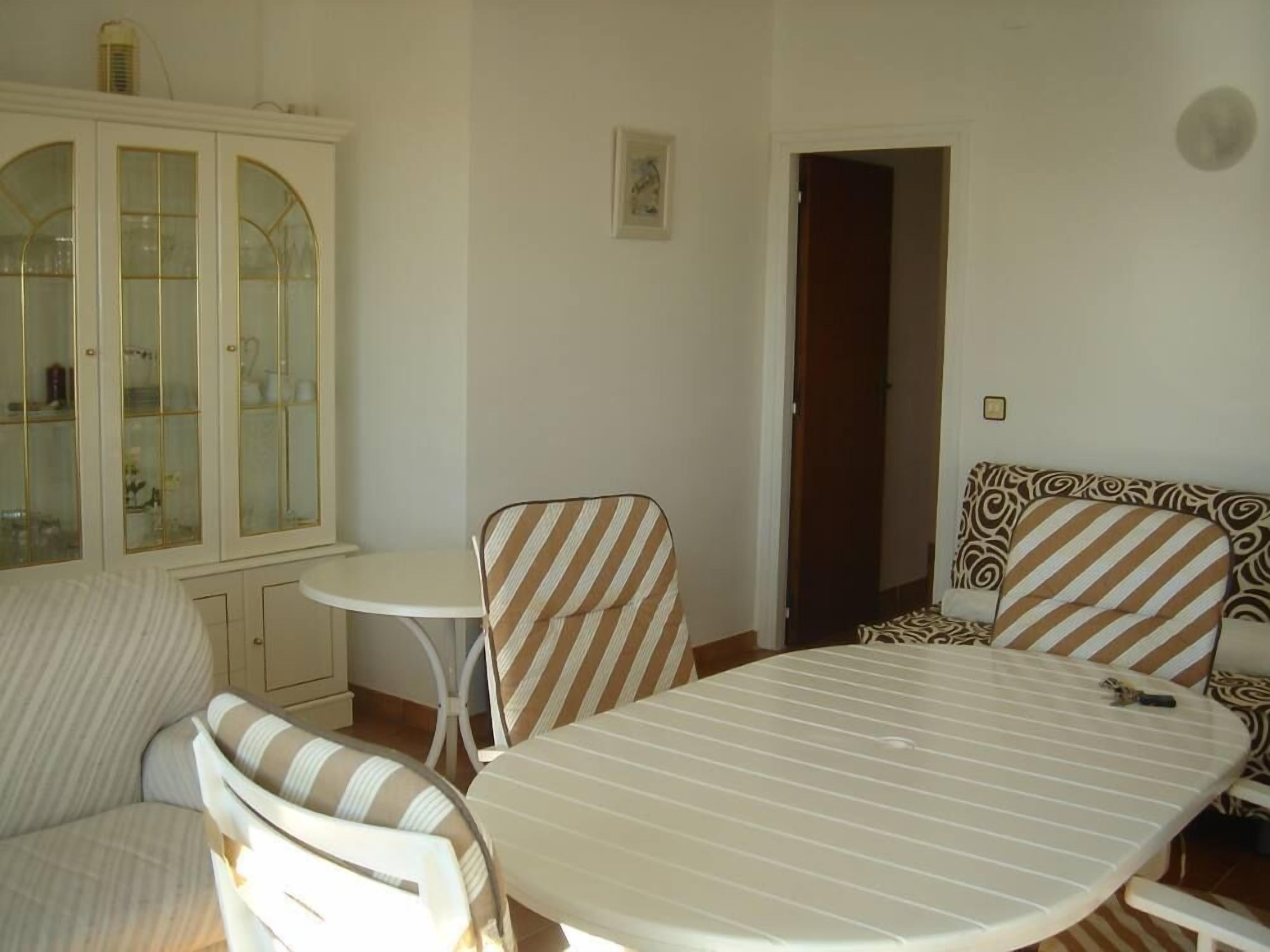 A room with a round table, striped chairs, a cabinet with glass doors, and a patterned sofa.