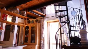 A rustic interior with wooden beams, a spiral staircase, and shelves with various items.