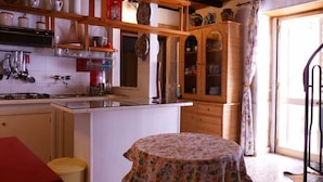 A kitchen with wooden shelves, a dining table with a floral tablecloth, and a cabinet with glass doors.