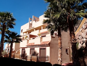 Stunning multi-story building with a flat roof and balconies, surrounded by palm trees and a wooden fence.