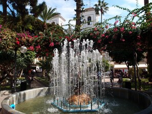Stunning public fountain surrounded by lush greenery and flowering plants, set against a historic backdrop.