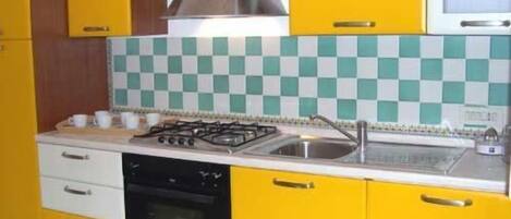 A kitchen with yellow cabinets, a gas stove, a sink, and a microwave.