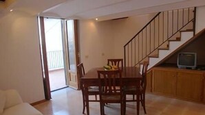 A dining area with a wooden table and chairs, a television on a wooden cabinet, and a staircase leading to an upper floor.