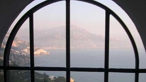 A view through a window with a metal frame, overlooking a coastal area with buildings and a body of water.