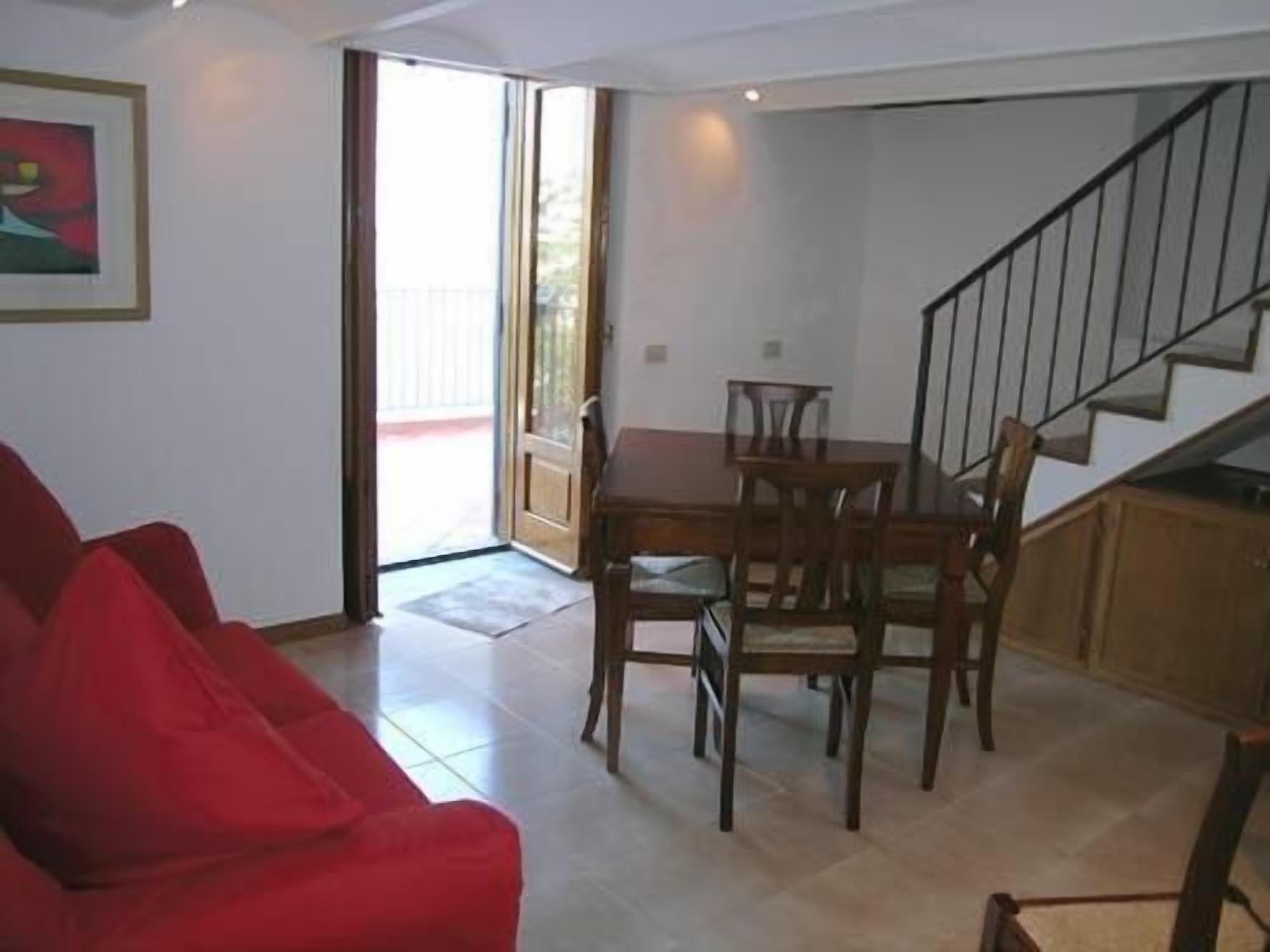 A living room with a red sofa, a dining table with chairs, and a staircase.