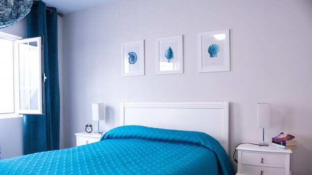 Een slaapkamer met een bed, een nachtkastje, een lamp en drie ingelijste foto’s aan de muur.