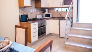 Een compacte keuken met een kookplaat, magnetron en oven. Er staat een eettafel met stoelen en een mandje op.