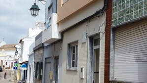 Een straat met gebouwen, waaronder een gebouw met twee verdiepingen en een balkon, en een winkel met een gesloten luik.