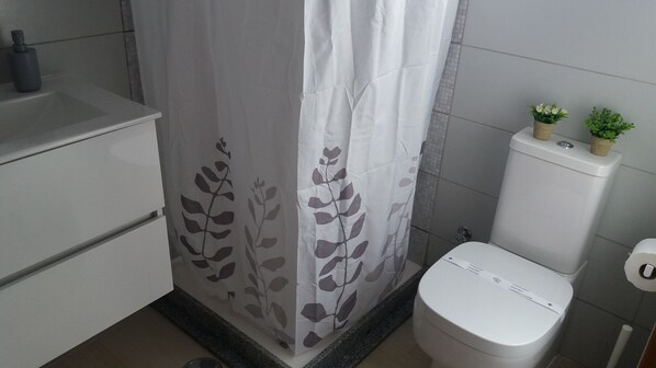 A bathroom with a toilet, a sink, and a shower curtain with a leaf pattern. - Casa António B (Alvor)